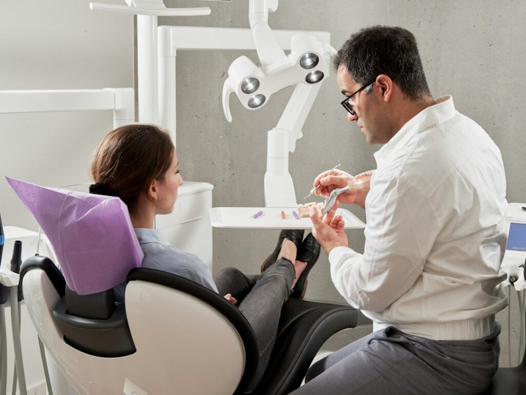 Older adult reviewing a dental implant model with a clinician in a bright treatment room.