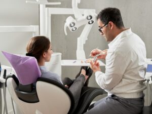 Older adult reviewing a dental implant model with a clinician in a bright treatment room.